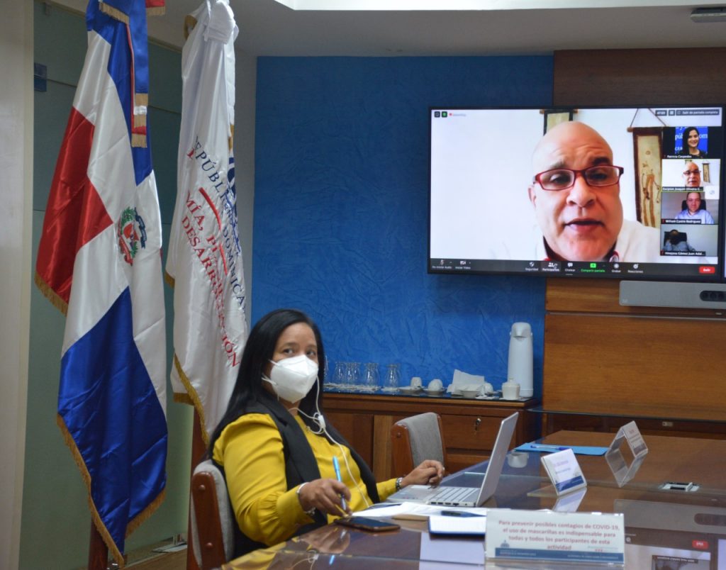 Lidia Encarnación, directora de Cooperación Regional del Ministerio de Economía, Planificacion y Desarrollo, en pantalla Escipión Oliveira secretario general adjunto para comercio y transformación económica sostenible, de la Organización de Estados del Caribe, África y Pacifico (OEACP).