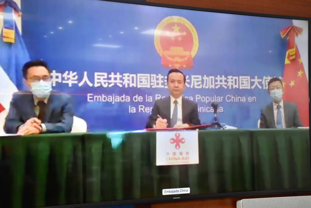 El ministro de Economía, Planificación y Desarrollo, Miguel Ceara Hatton, y el embajador de la República Popular China en el país, Zhang Run firman el acta de entrega de donación de material antiepidémico. Cada uno en sus sedes ministeriales y diplomáticas. 